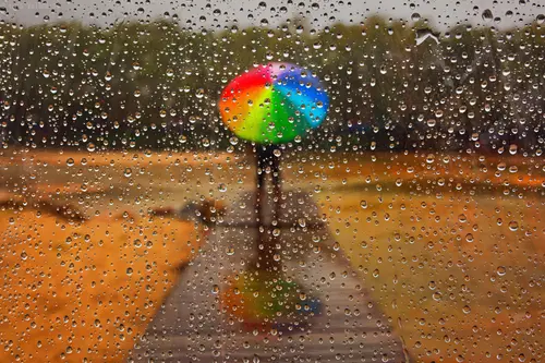 Image "A man with a multicolored umbrella, standing on a wet path in the rain" (3240x2160)