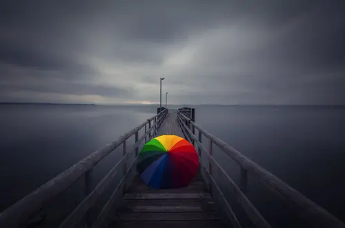 Image "There is a bright rainbow umbrella on the pier, stretching into the gray sea" (2048x1357)